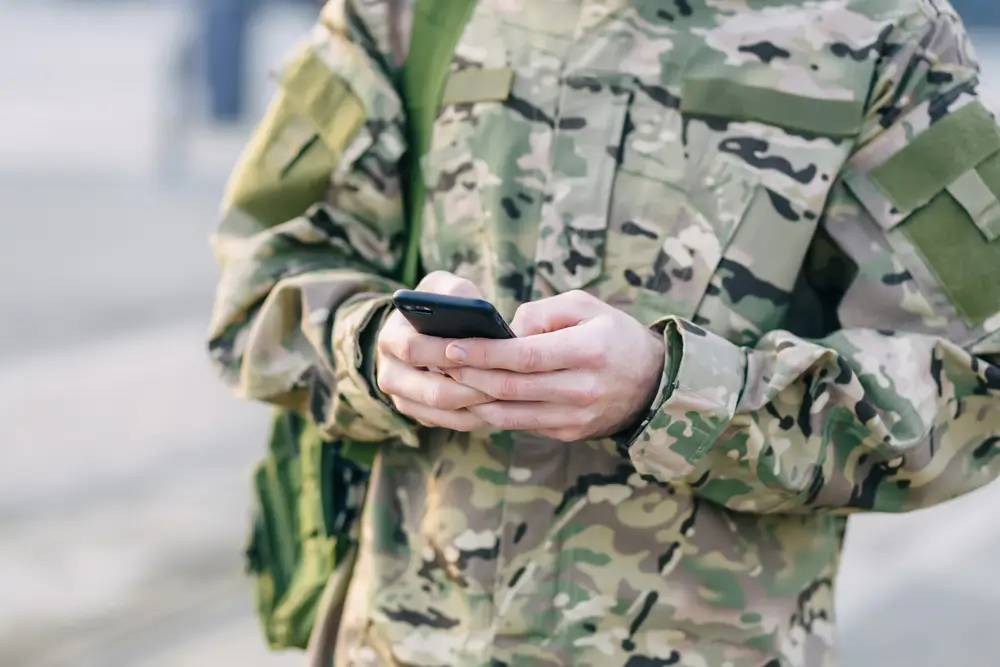 Carabiniere in divisa militare utilizza lo smartphone per esercitarsi con il simulatore dei quiz per i concorsi.