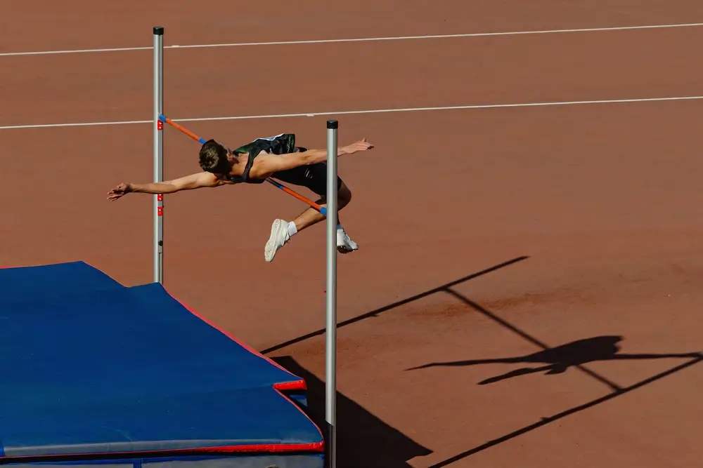 Atleta che esegue un salto in alto superando l'asticella con la tecnica Fosbury durante una prova di atletica.