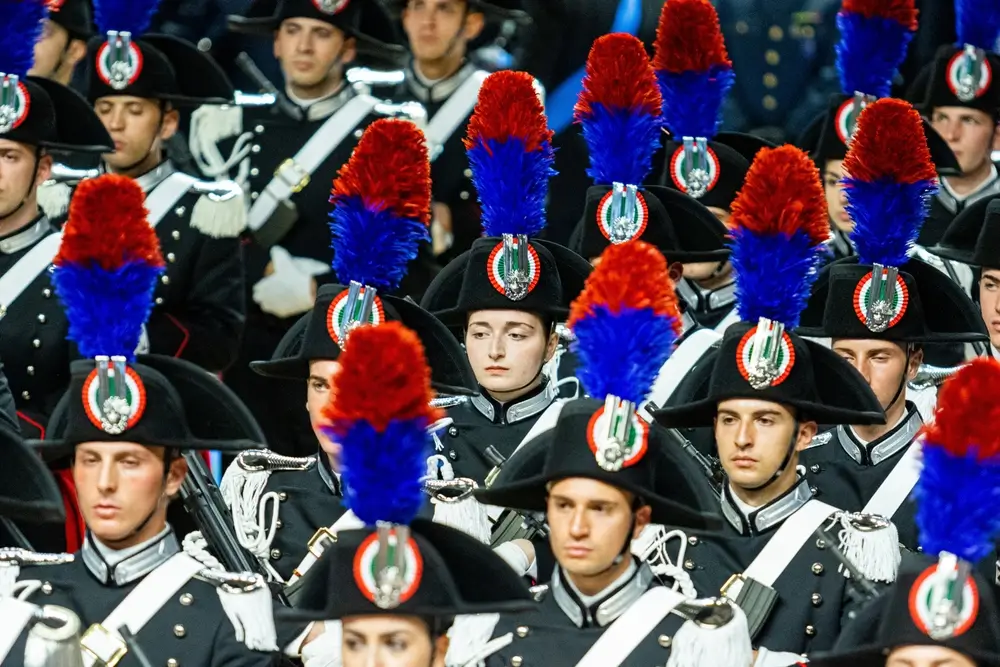 Carabinieri in uniforme da cerimonia con cappello a lucerna e pennacchio rosso e blu durante un evento solenne dell'Arma.