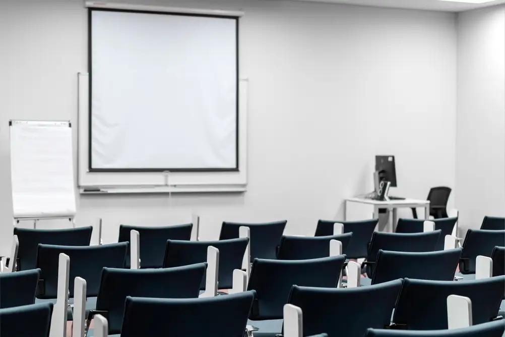 Aula formazione moderna della scuola ufficiali con file di sedie blu, schermo per proiezioni e postazione computer.
