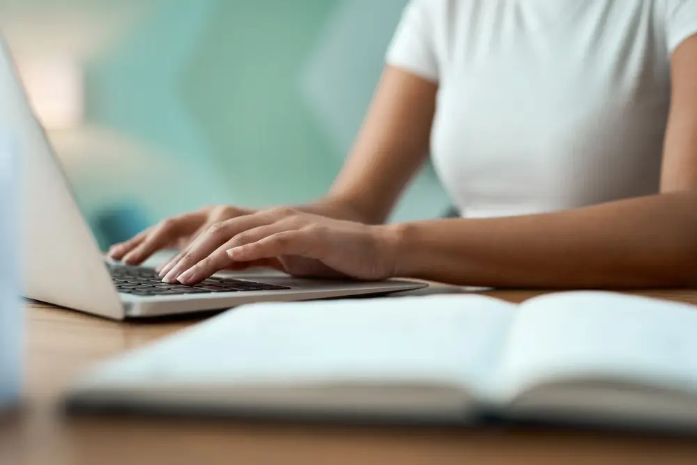 Studente che usa un computer per la preparazione ai test di concorso, con un libro aperto in primo piano.