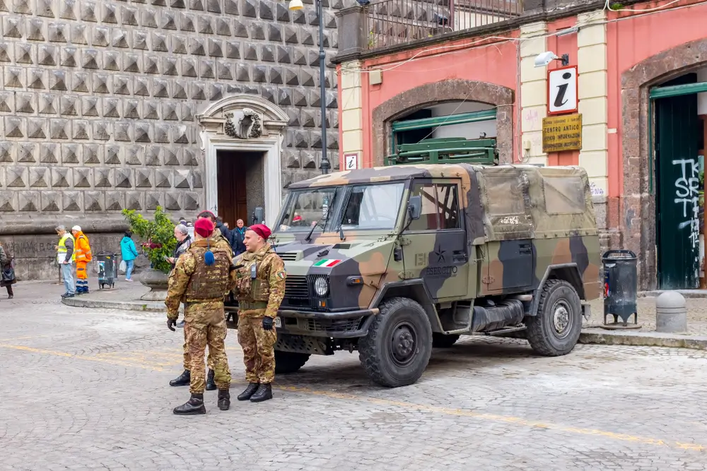 Carabinieri in divisa mimetica e basco rosso vicino a un mezzo militare durante l'addestramento in caserma.