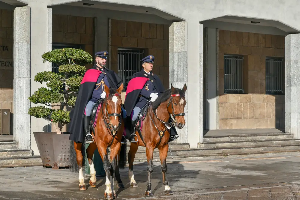 Due carabinieri forestali a cavallo in alta uniforme con mantello durante un servizio di pattugliamento.