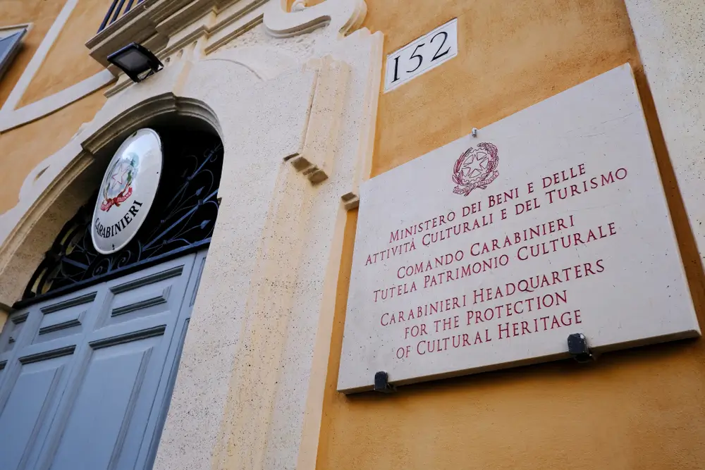 Ingresso di una caserma dei Carabinieri con lo stemma dell'Arma sopra il portone e targa del comando su muro ocra.