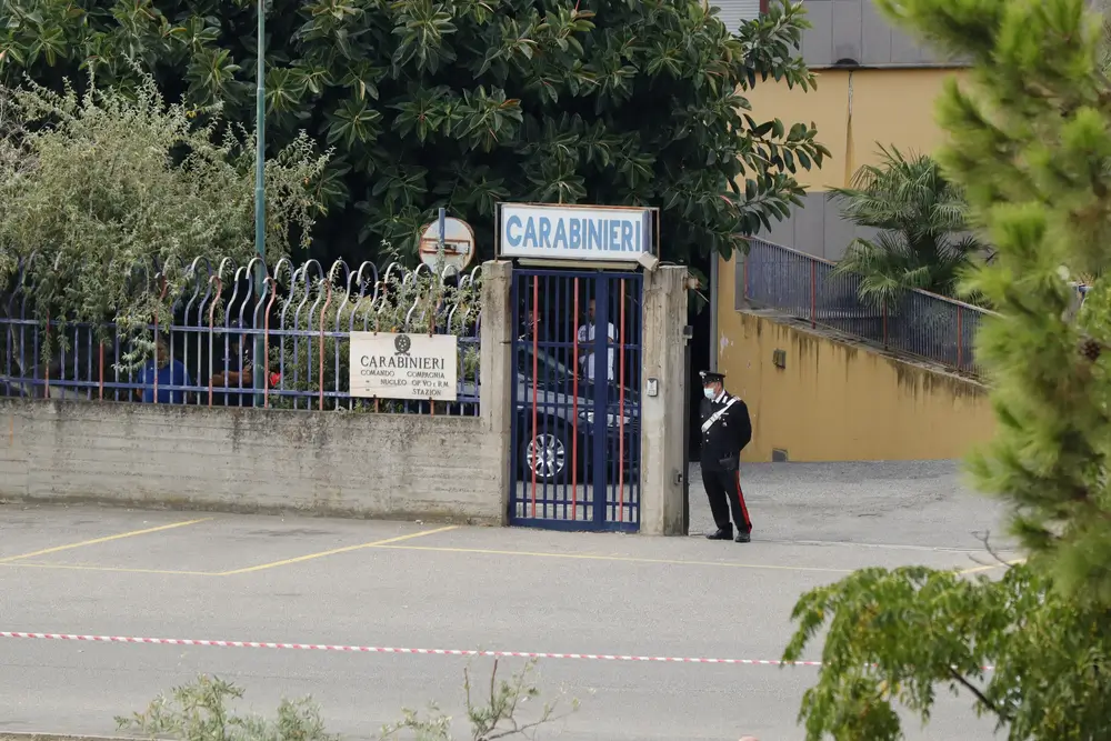Ingresso di una caserma dei Carabinieri con un militare in divisa davanti al cancello e l'insegna del comando stazione.