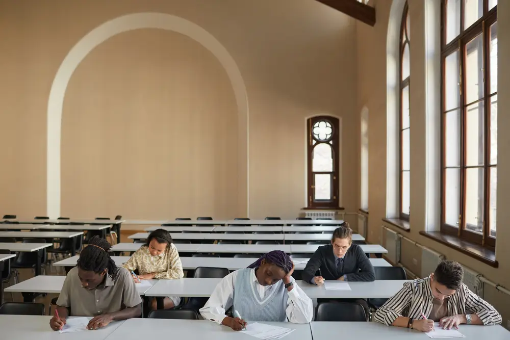 Candidati concentrati mentre svolgono una prova scritta seduti ai banchi di un'aula durante un concorso.
