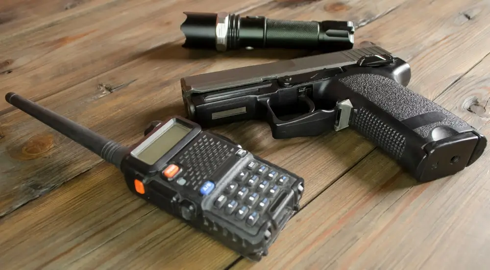 Equipaggiamento tattico dei Carabinieri con pistola, ricetrasmittente e torcia su un tavolo di legno.