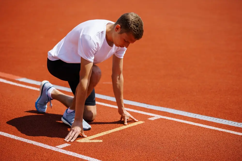 Giovane atleta in posizione di partenza sulla pista rossa durante la prova di efficienza fisica del concorso.