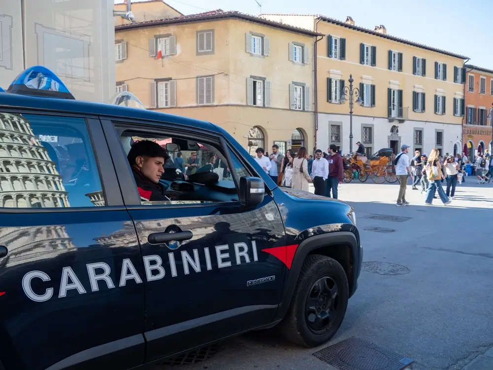 Ufficiale dei Carabinieri in servizio operativo a bordo di un'auto d'ordinanza in una piazza storica.