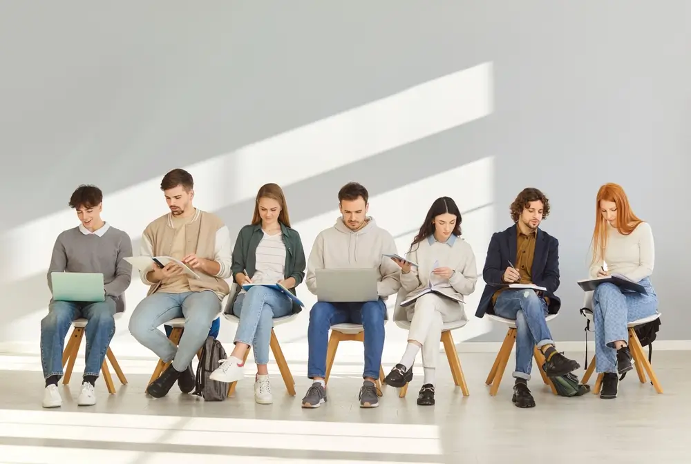Candidati seduti in fila studiano su laptop e appunti in attesa delle prove del concorso Allievi Marescialli.