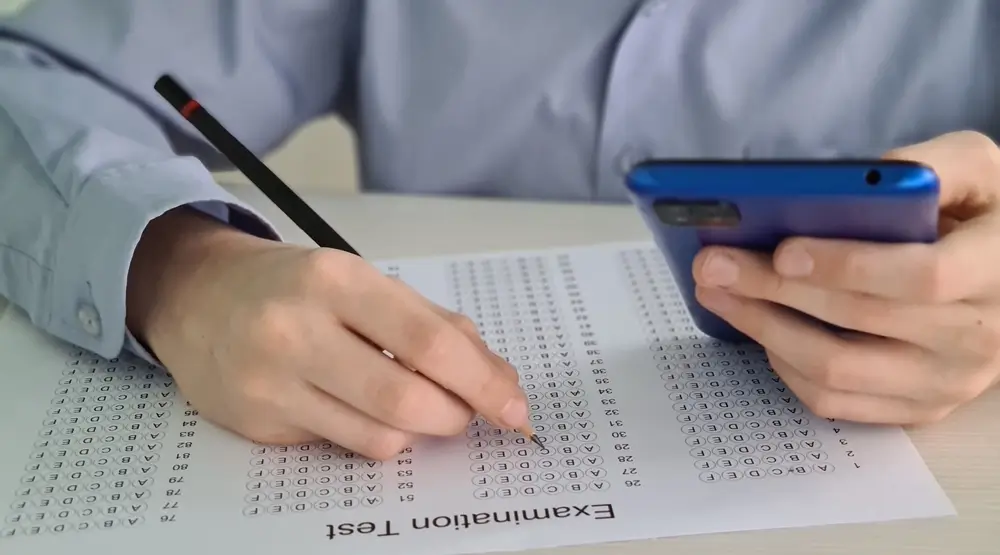 Studente che usa lo smartphone mentre compila un modulo per quiz a scelta multipla per prepararsi a un esame.