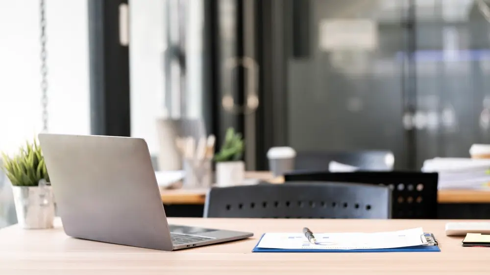 Laptop aperto su una scrivania da ufficio con documenti, ideale per esercitarsi online sui quesiti del concorso.