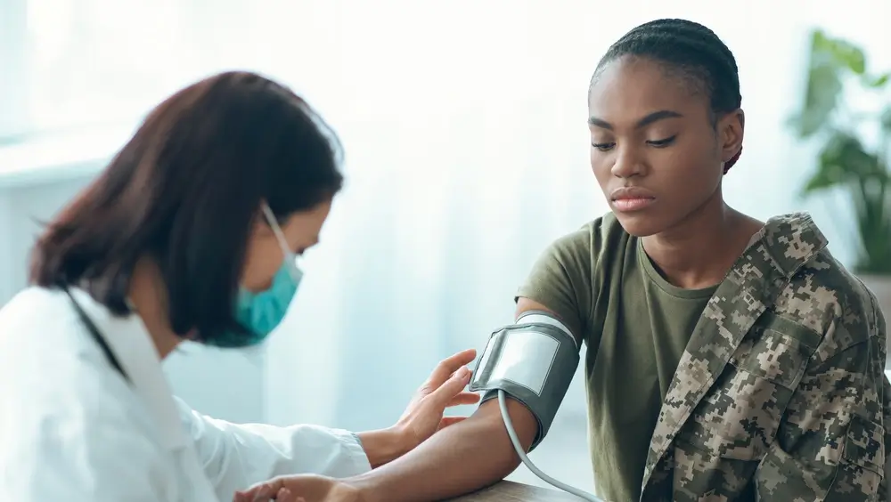 Medico che misura la pressione a una candidata in divisa mimetica durante la visita medica militare.