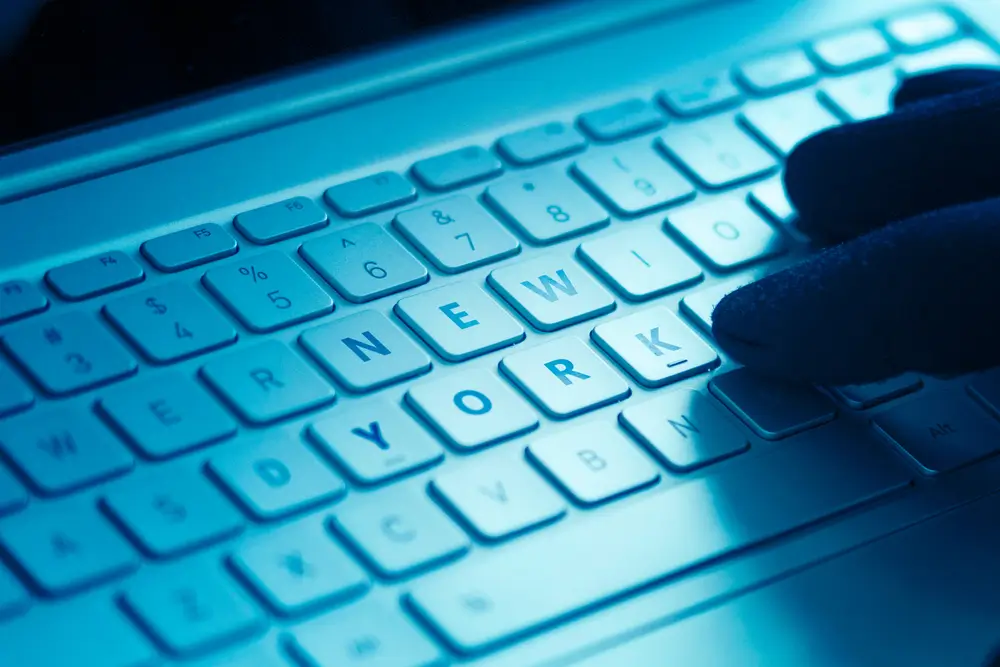 Dita guantate su una tastiera di computer illuminata di blu, a simboleggiare il pericolo di una email sospetta.