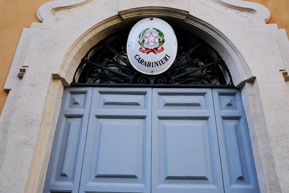 Ingresso di una caserma dei Carabinieri con portone azzurro e stemma ufficiale della Repubblica Italiana.