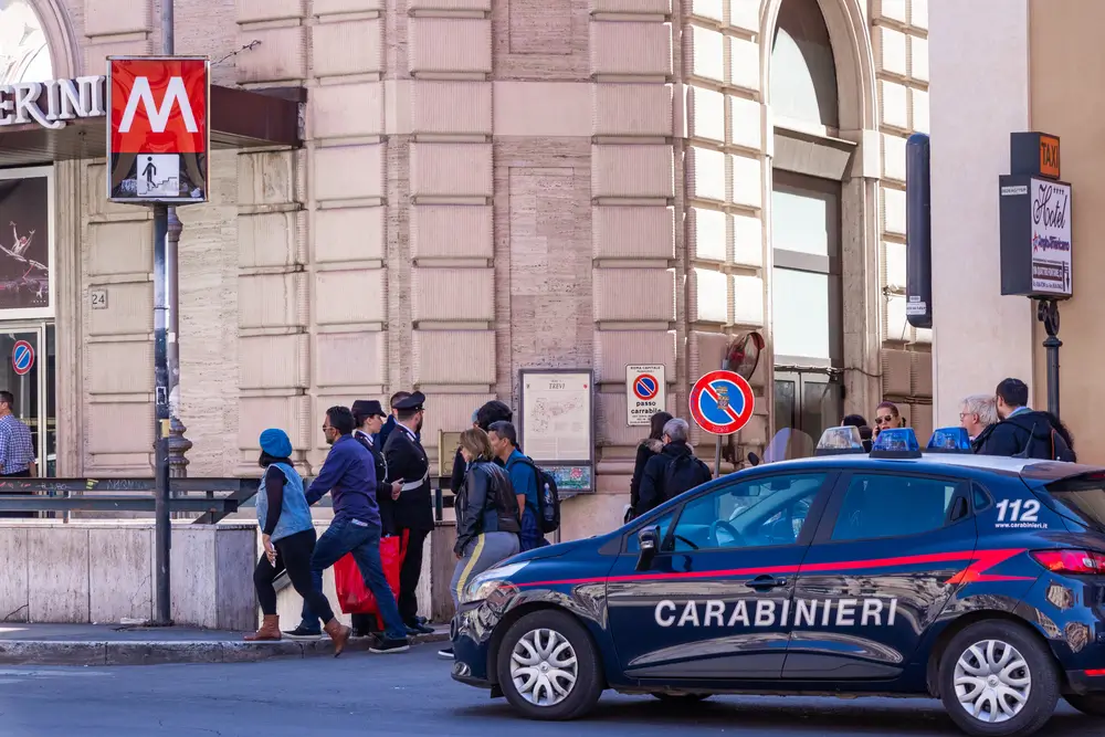 Due Carabinieri pattugliano una piazza cittadina accanto a un'auto d'ordinanza per la sicurezza urbana.